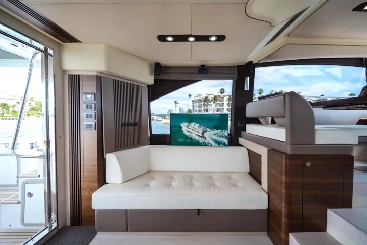 Modern yacht interior with white couch, wooden accents, and a large window view of the water and buildings.
