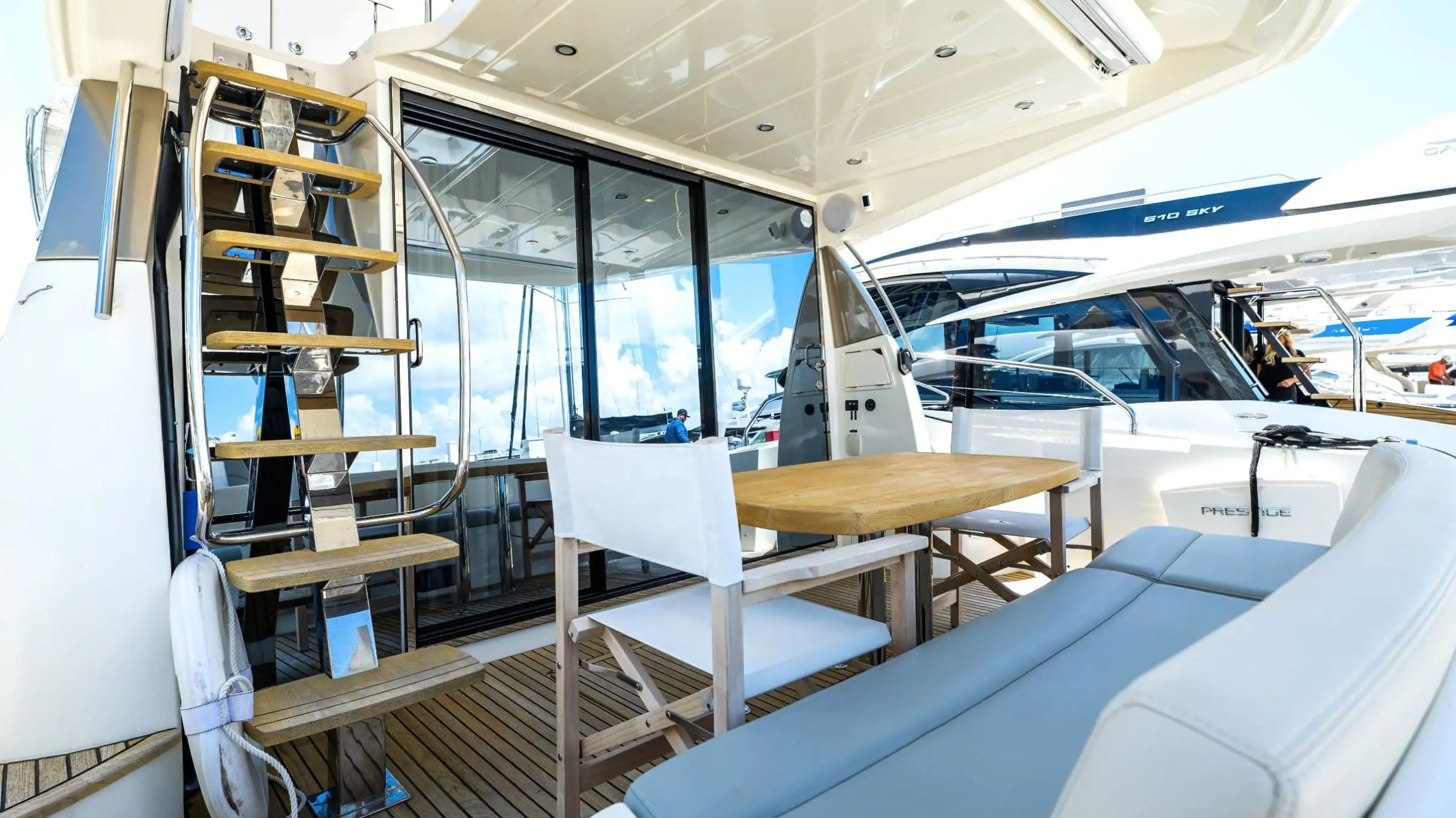 Luxury yacht deck with wooden stairs, seating area, and glass doors.