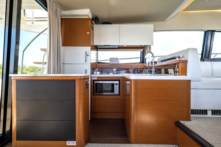 Modern yacht kitchen with wood cabinets, microwave, and sink, near large windows and stairs.