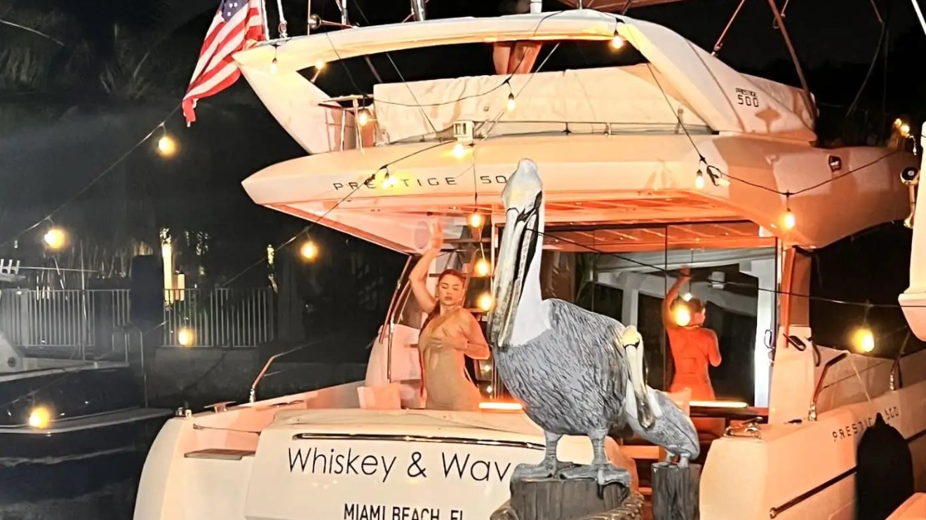 People on a yacht at night with string lights and a pelican statue in the foreground.