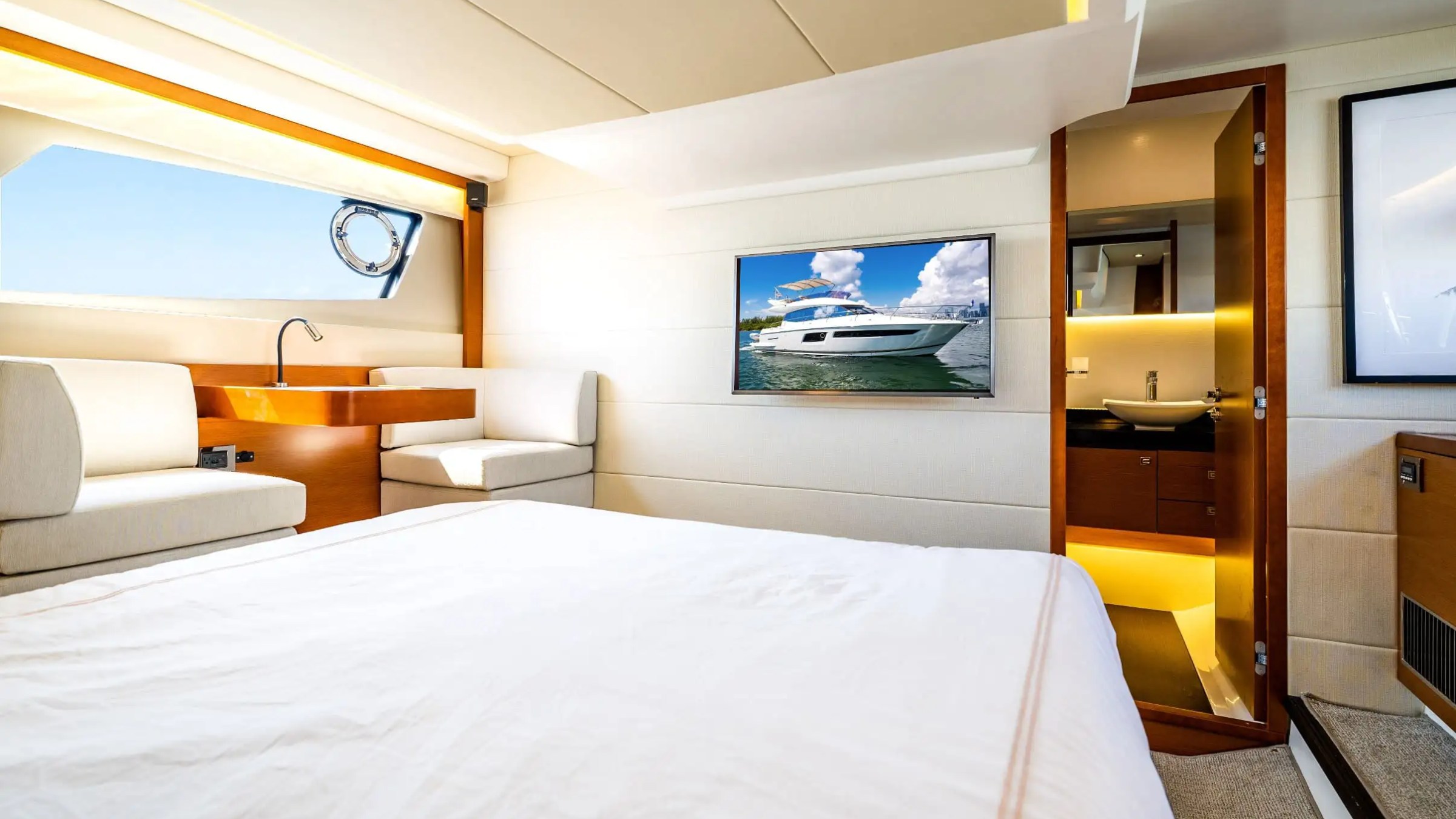 Luxury yacht bedroom with bed, TV showing a yacht, seating, and bathroom view.