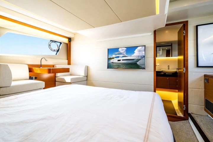 Luxury yacht bedroom with bed, TV showing a yacht, seating, and bathroom view.