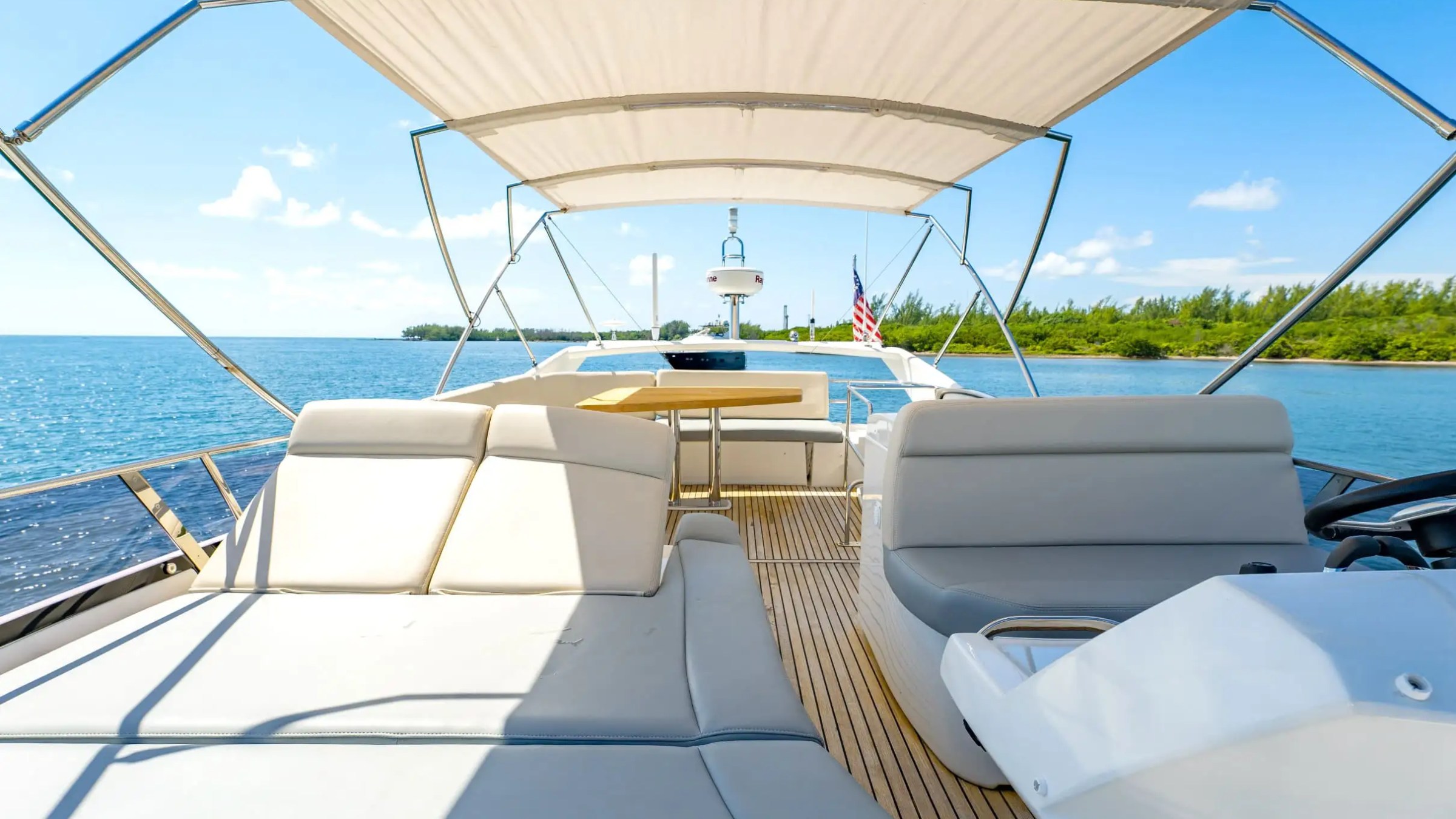 View from yacht deck with sun shade, seating, table, overlooking water and distant shoreline.