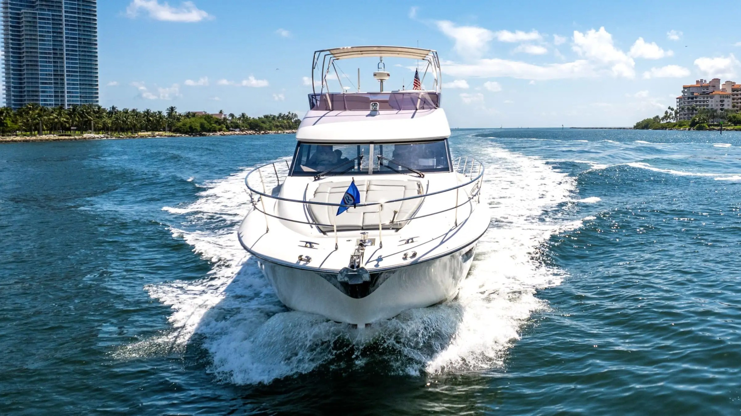 Large white yacht cruising on blue water with city skyline in background.