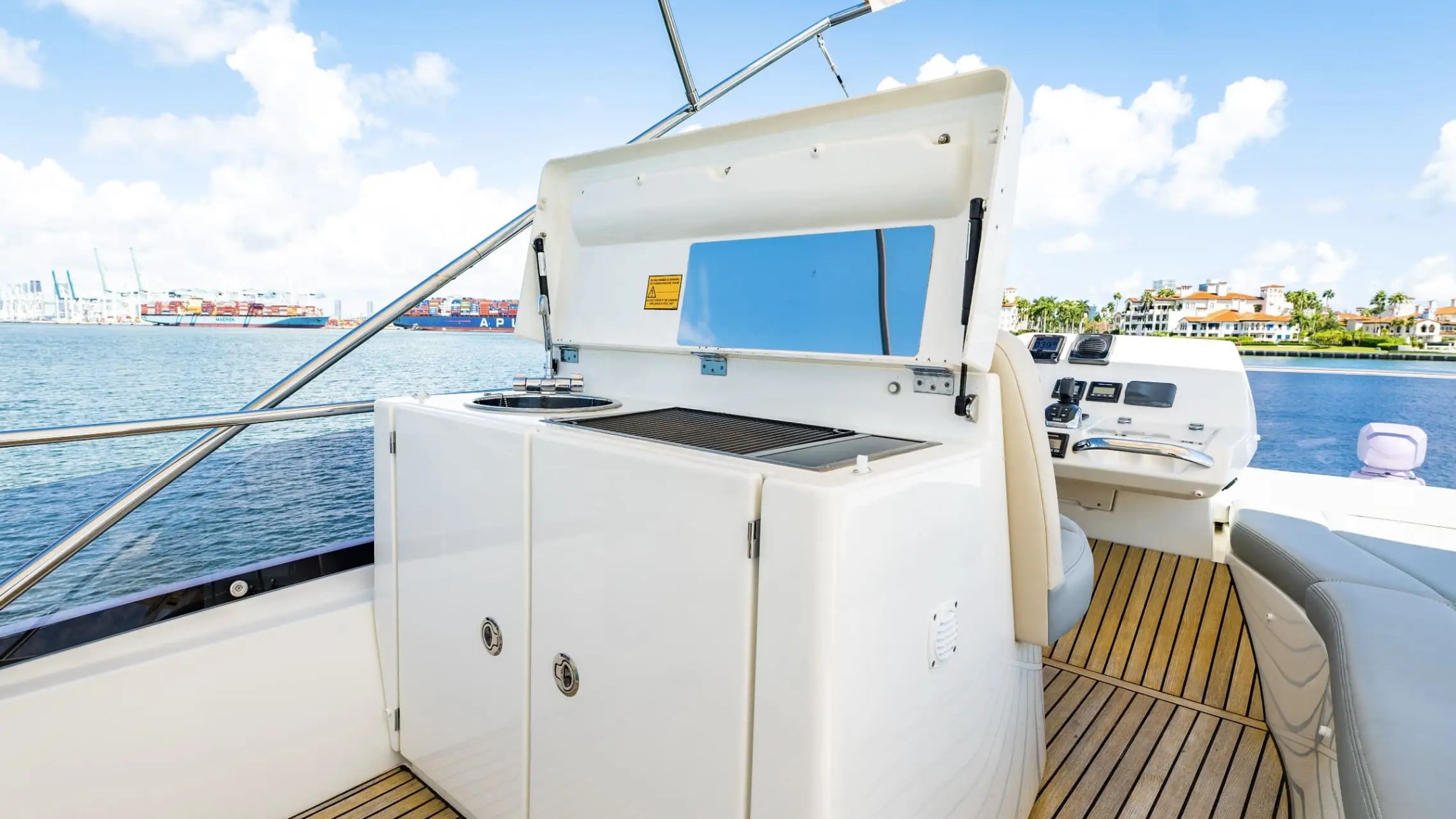 Boat deck with grill, seating, and ocean view under a bright blue sky.