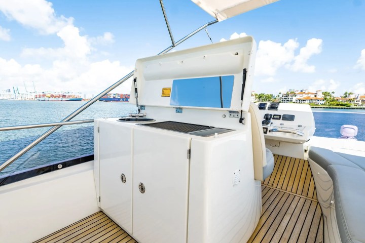 Boat deck with grill, seating, and ocean view under a bright blue sky.