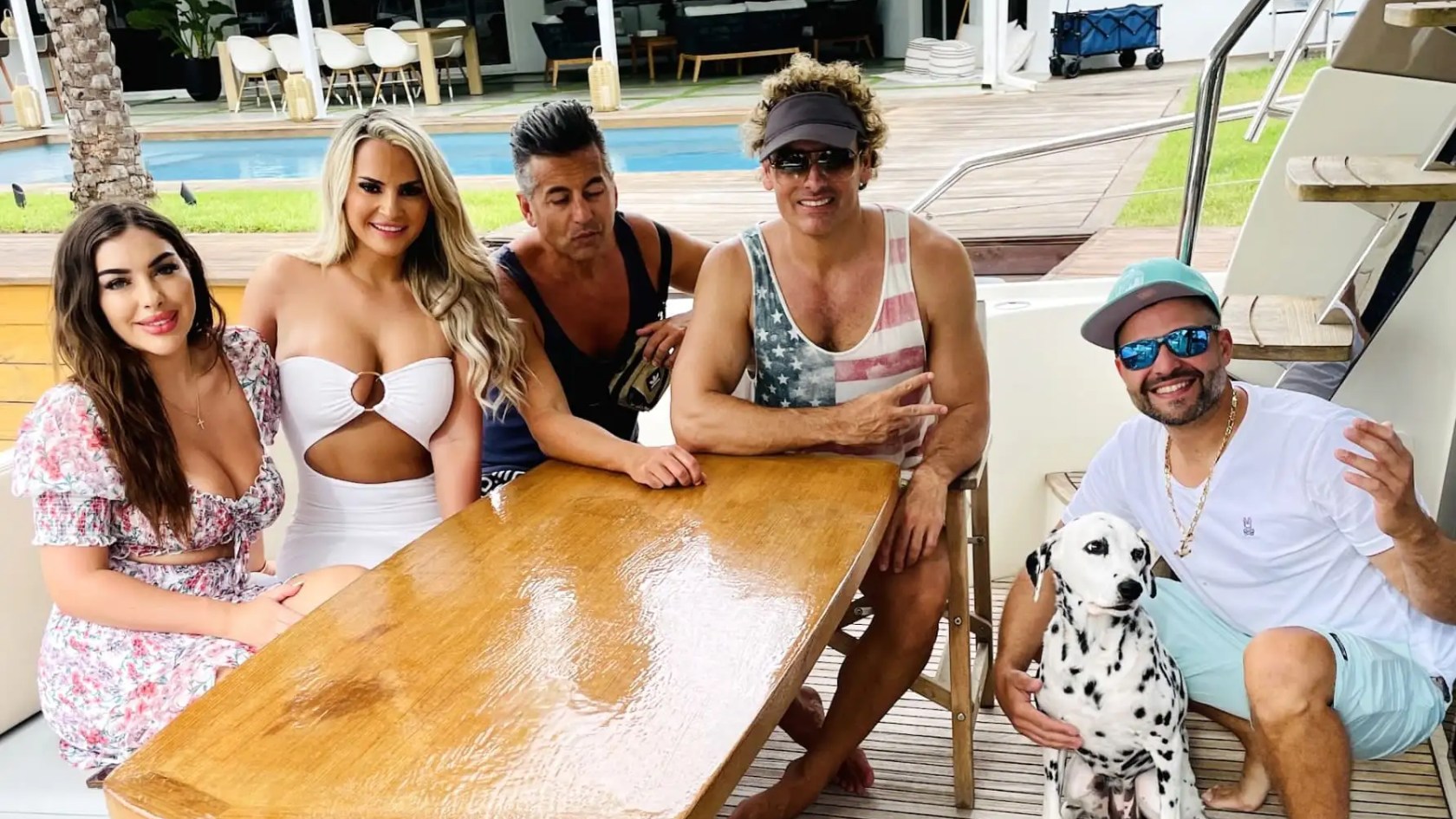 Five people and a Dalmatian sitting around a wooden table on a boat.