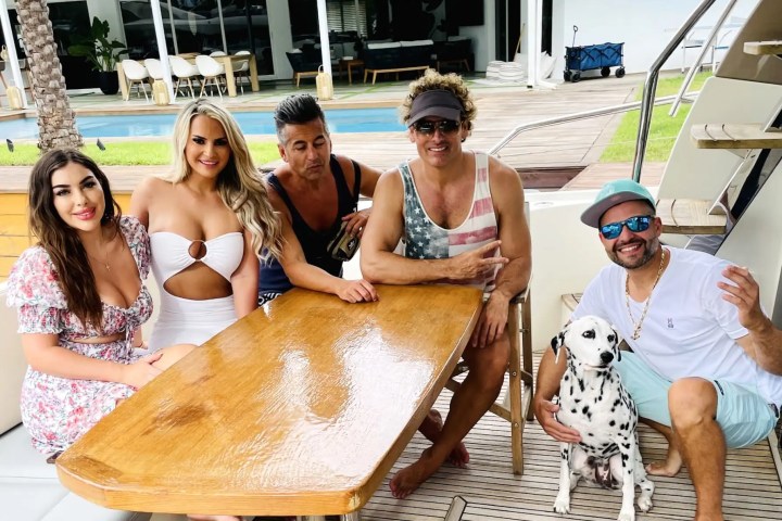 Five people and a Dalmatian sitting around a wooden table on a boat.