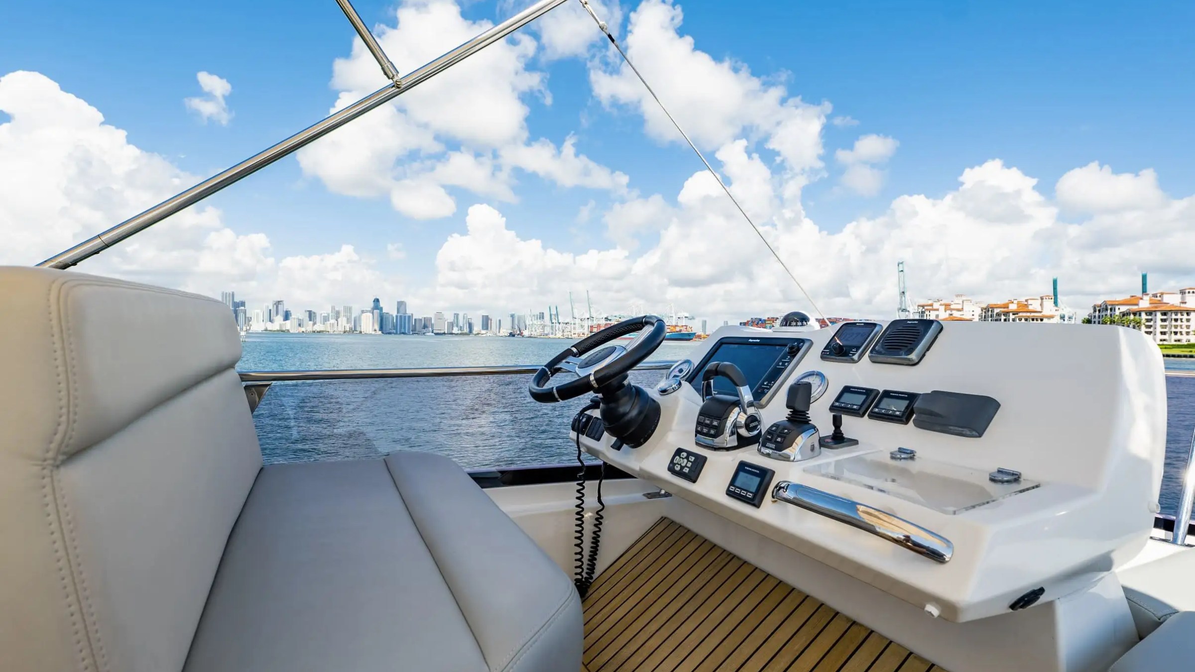Boat steering area with controls, overlooking a city skyline and ocean under a blue sky with clouds.