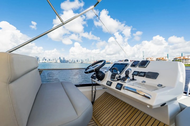 Boat steering area with controls, overlooking a city skyline and ocean under a blue sky with clouds.
