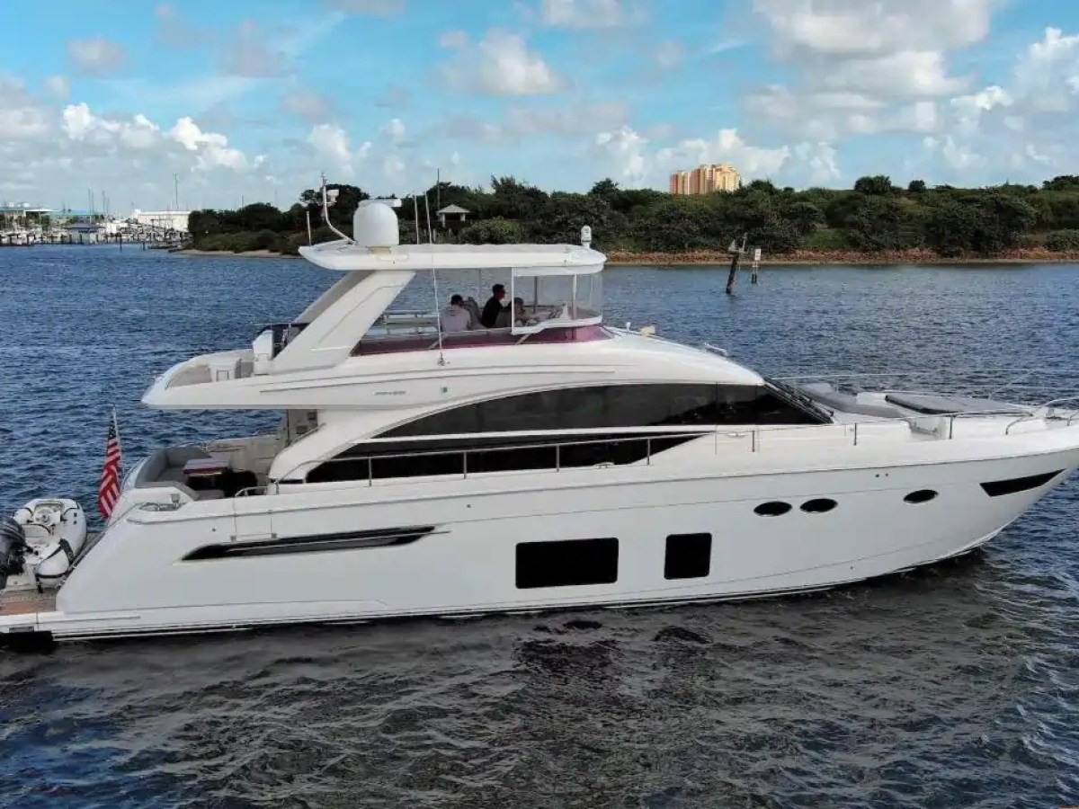 White yacht cruising on water with an American flag, clear sky and greenery in background.