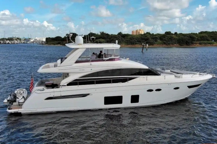 White yacht cruising on water with an American flag, clear sky and greenery in background.