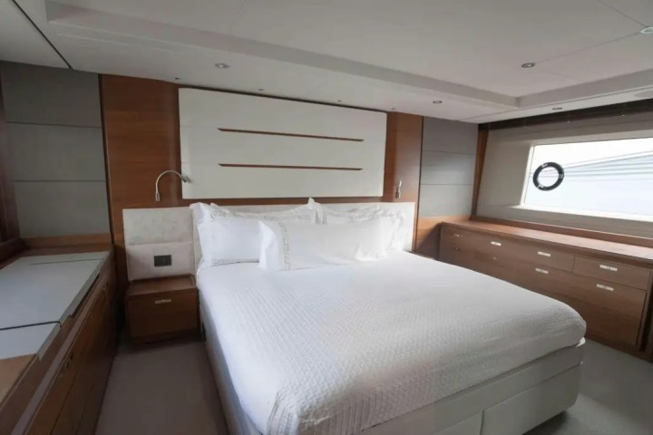 Modern bedroom with a large bed, white linens, wood paneling, and a porthole window.