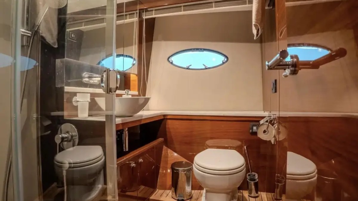 Boat restroom with toilet, sink, shower, wooden floor, and oval windows.