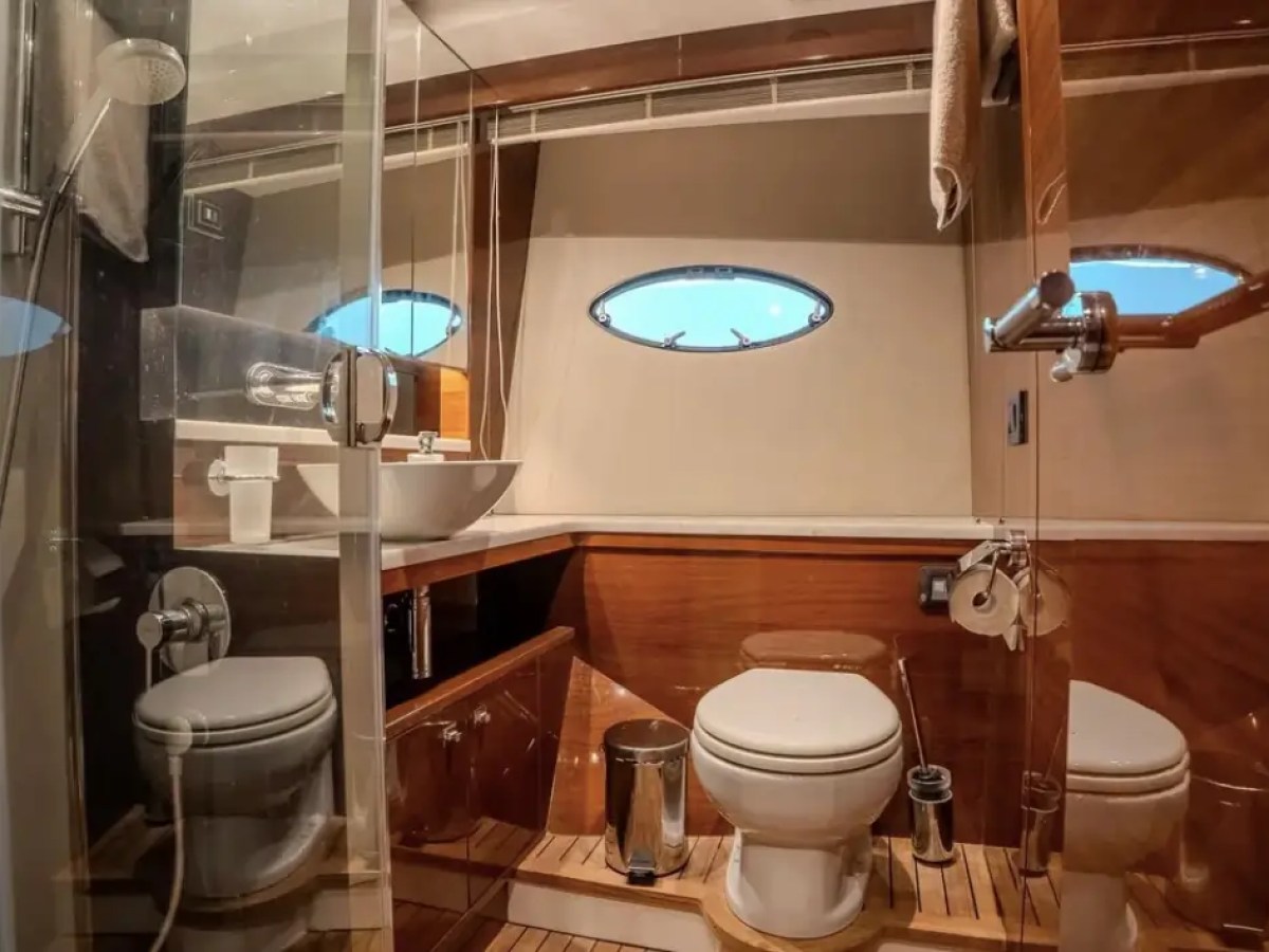Boat restroom with toilet, sink, shower, wooden floor, and oval windows.