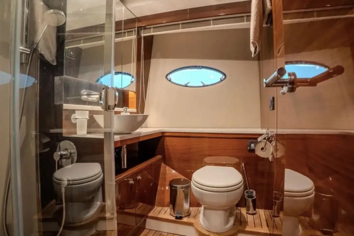 Boat restroom with toilet, sink, shower, wooden floor, and oval windows.