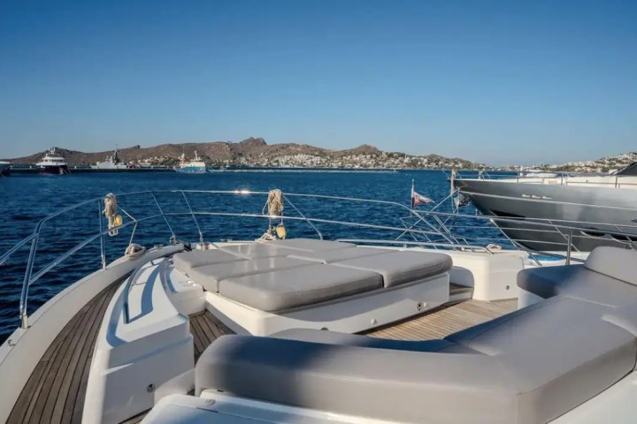 Private yacht deck with sun loungers overlooking a harbor and hills under a clear blue sky.