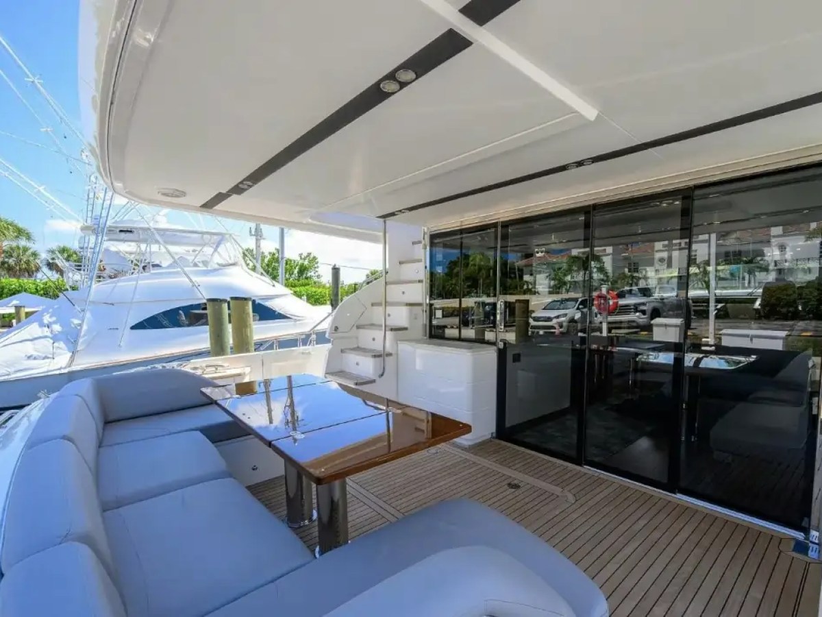 Luxury yacht deck with seating, table, and sliding glass doors to interior, docked near palm trees.
