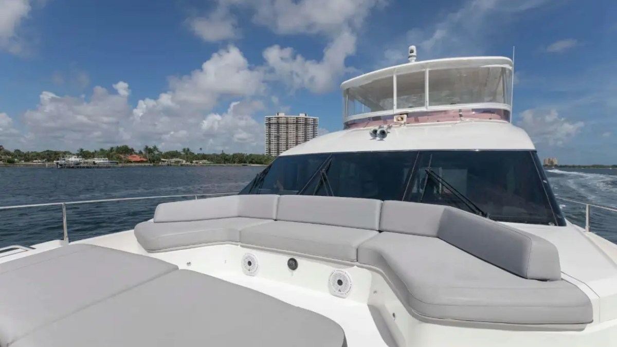 Luxury yacht's deck with cushioned seating, cruising near urban shoreline under a partly cloudy sky.