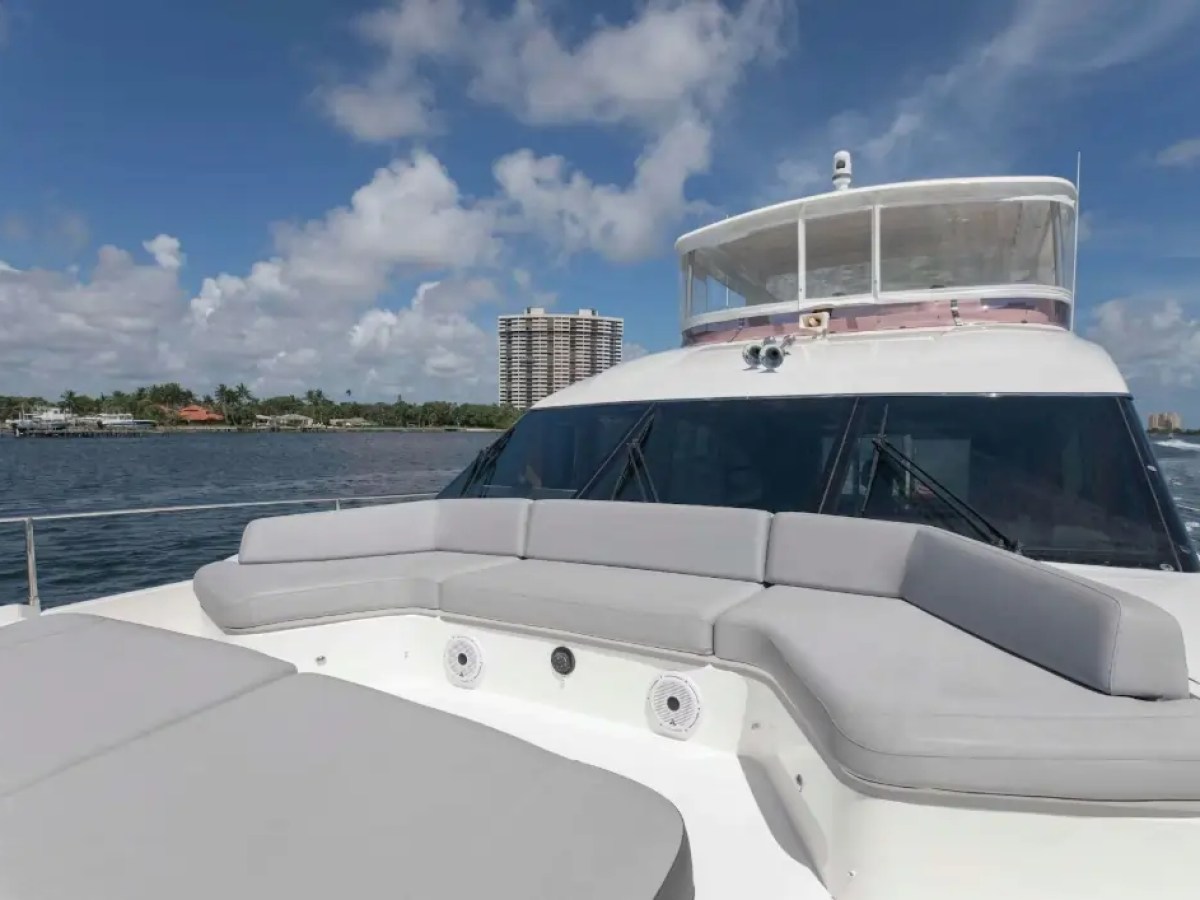 Luxury yacht's deck with cushioned seating, cruising near urban shoreline under a partly cloudy sky.