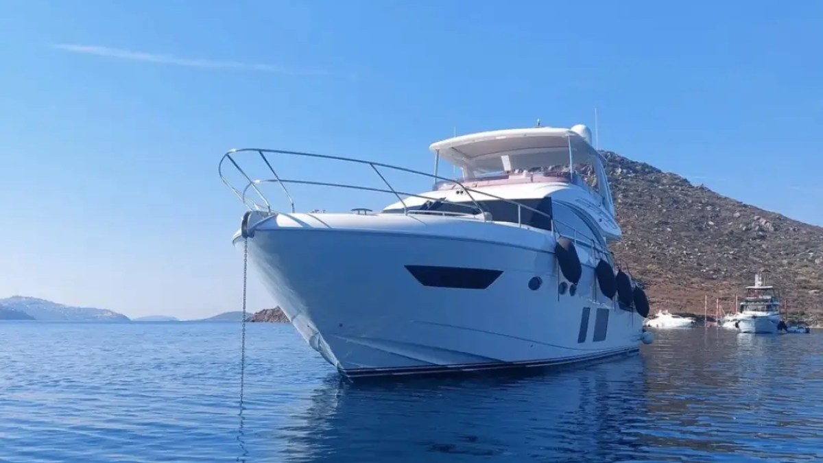 White yacht anchored on calm water with a clear blue sky and distant hills.