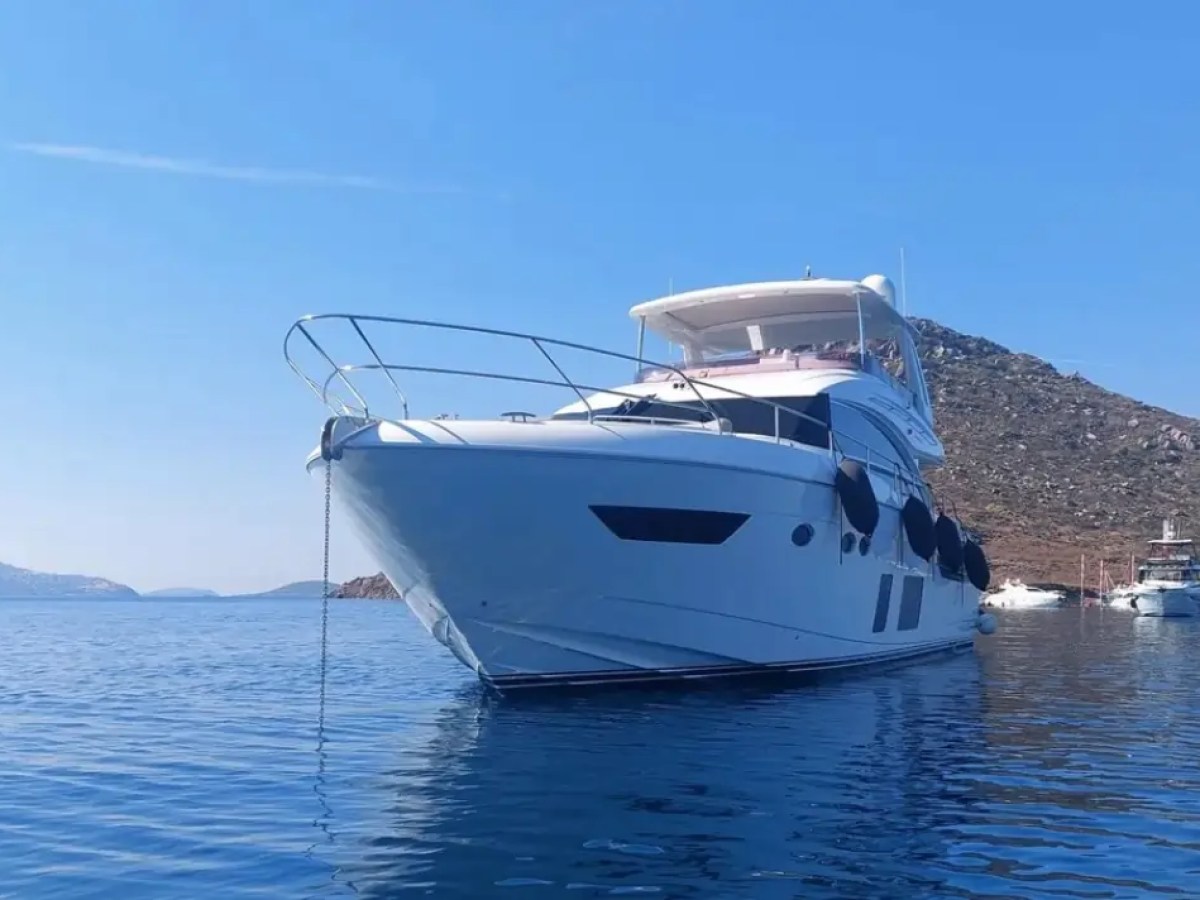 White yacht anchored on calm water with a clear blue sky and distant hills.