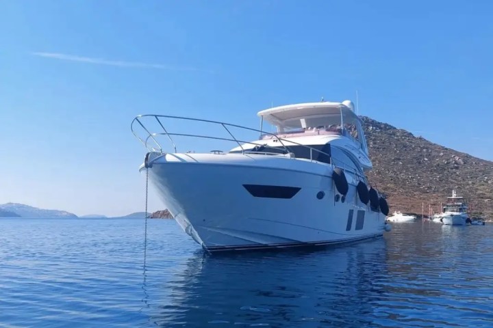 White yacht anchored on calm water with a clear blue sky and distant hills.
