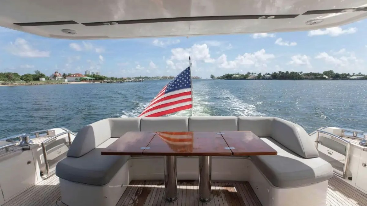 Rear deck of a yacht with seating, table, and American flag, overlooking the ocean.