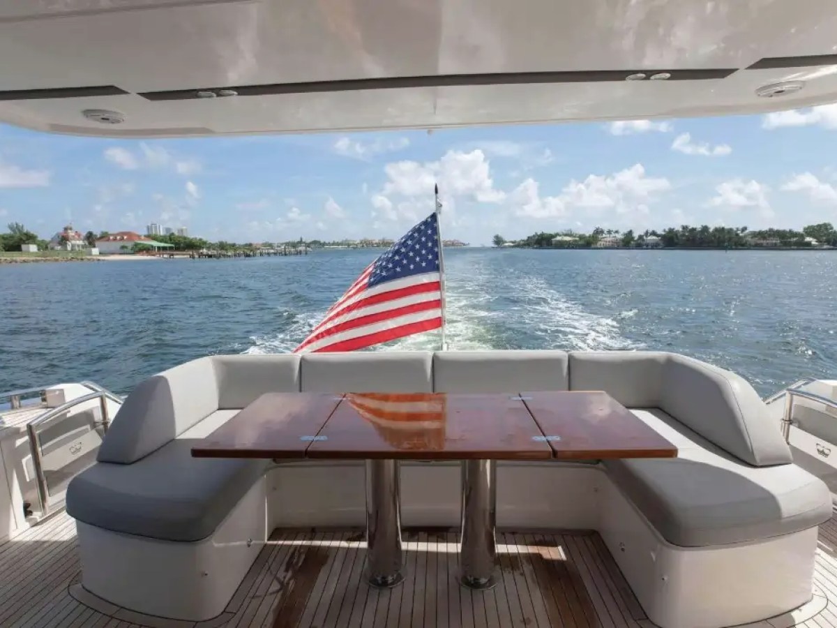 Rear deck of a yacht with seating, table, and American flag, overlooking the ocean.