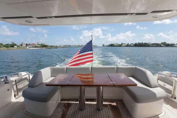 Rear deck of a yacht with seating, table, and American flag, overlooking the ocean.