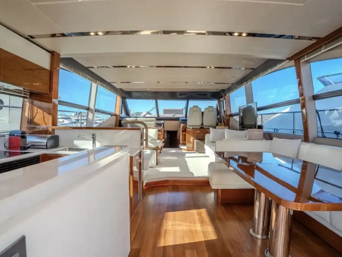 Luxurious yacht interior with white seating, wooden floors, and large windows showing a marina view.