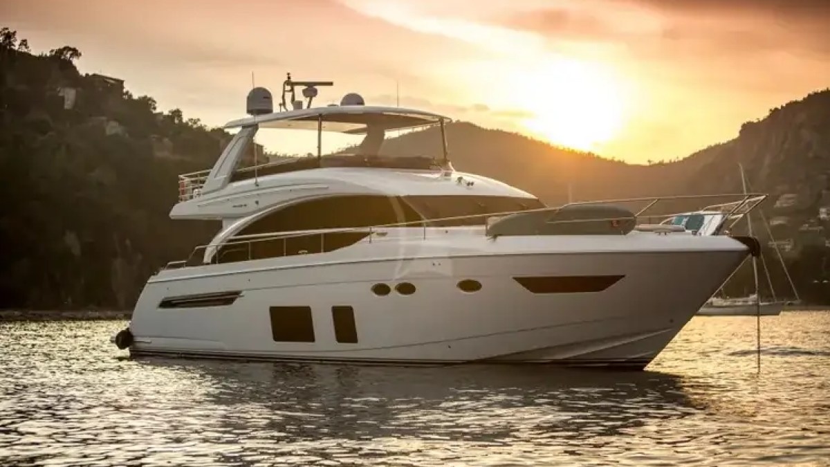 Luxury yacht on calm water at sunset near hills.