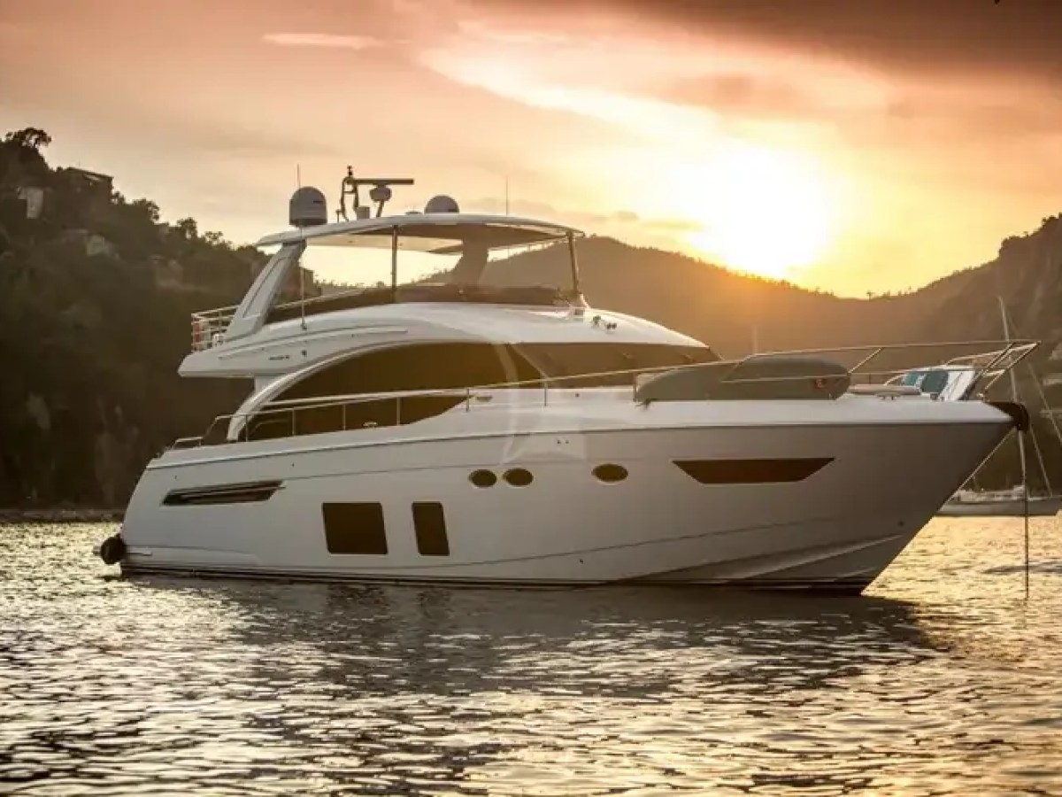 Luxury yacht on calm water at sunset near hills.