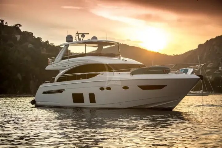 Luxury yacht on calm water at sunset near hills.