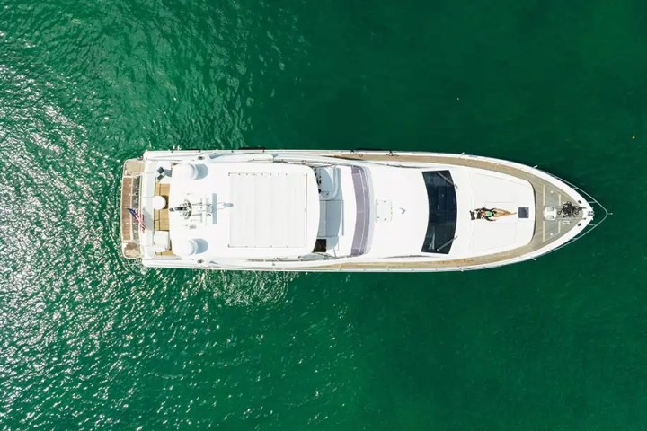 Overhead view of a white yacht on clear green water, person lounging on deck.