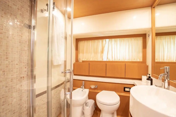 Modern bathroom with shower, toilet, and sink, featuring warm wood paneling and light beige tiles.