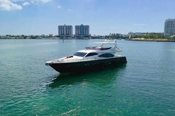A yacht on calm waters with city skyline in background under a clear blue sky.