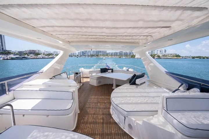 Spacious yacht deck with seating, tables, and ocean view against a city skyline.