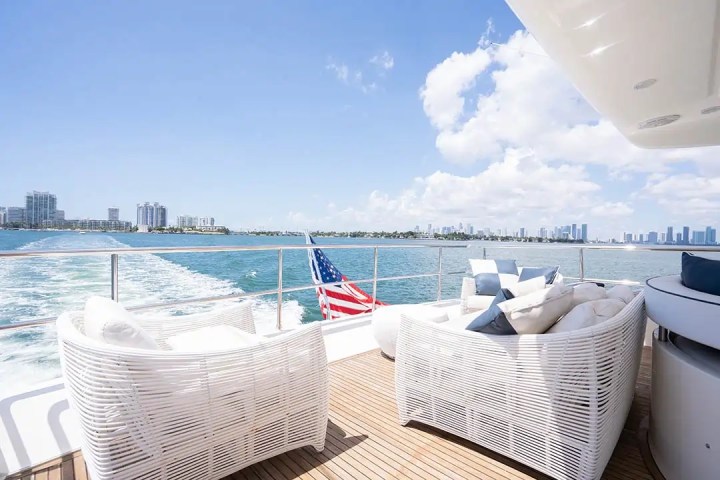 View from yacht deck with white seating, American flag, ocean, and skyline in background.