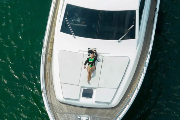 Aerial view of person in green swimsuit lounging on the deck of a white yacht in blue water.