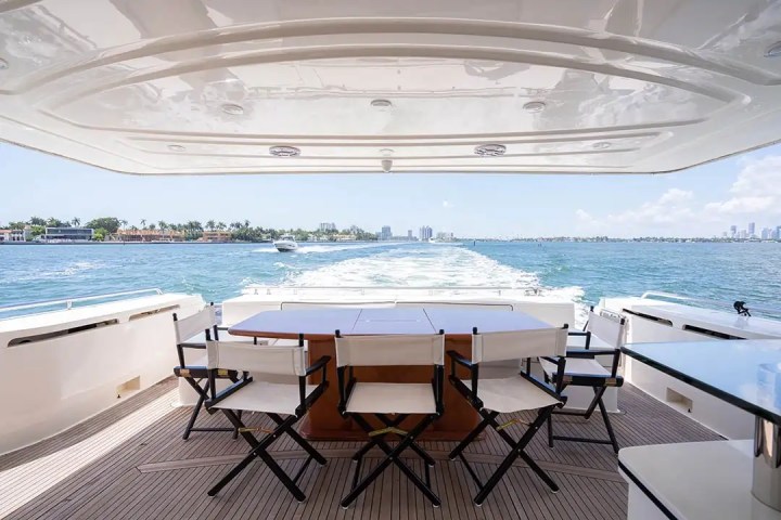 Back deck of a yacht with chairs and table, overlooking ocean waves and distant shoreline.