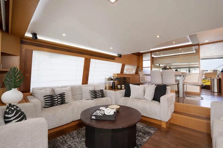 Luxurious yacht interior with beige sofas, round wooden table, and modern dining area in sleek design.