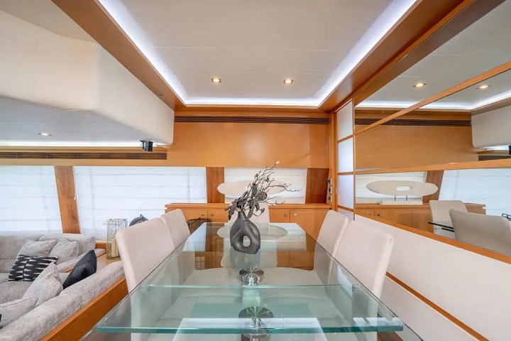 Modern yacht interior with glass dining table, white chairs, and decorative vase.