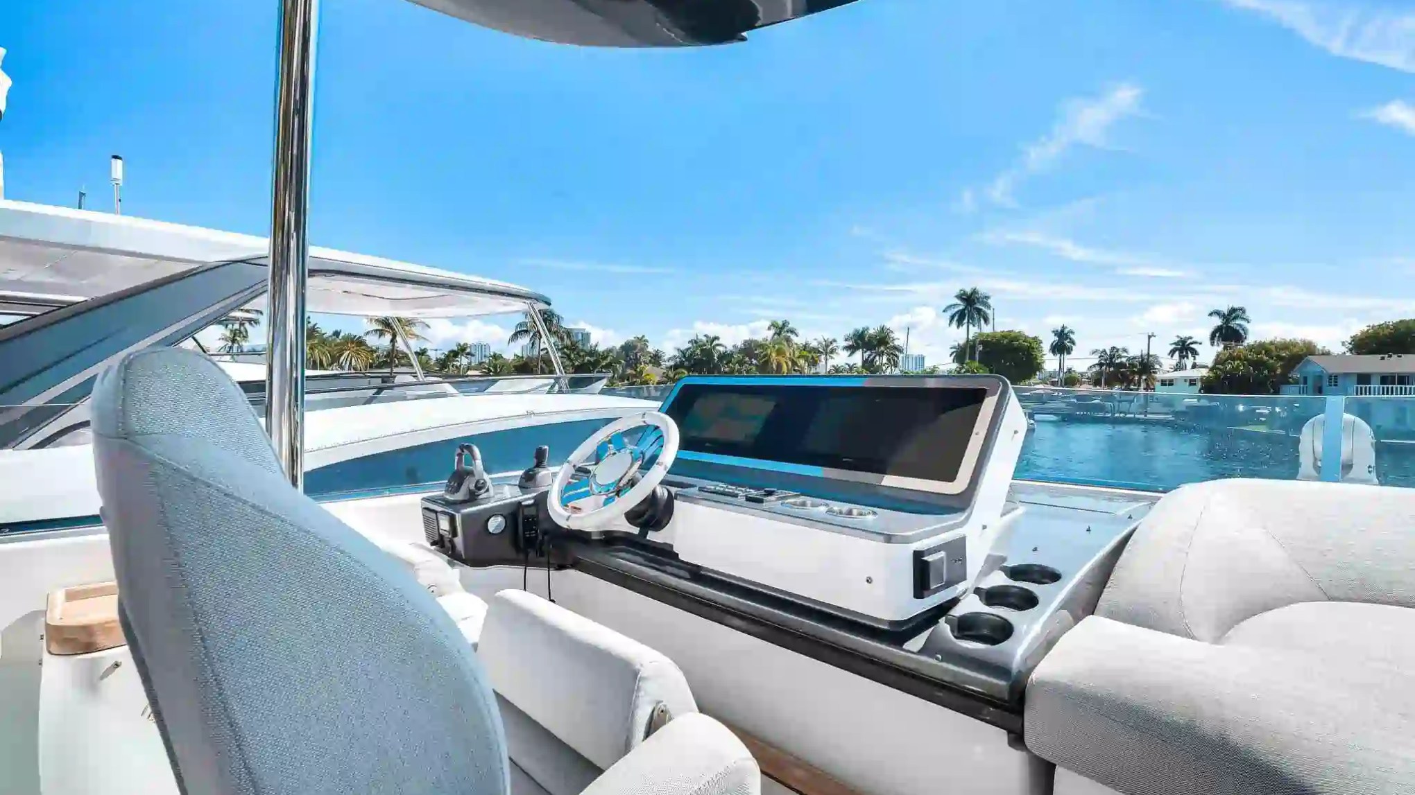 Boat cockpit with steering wheel and console overlooking water, palm trees, and blue sky.