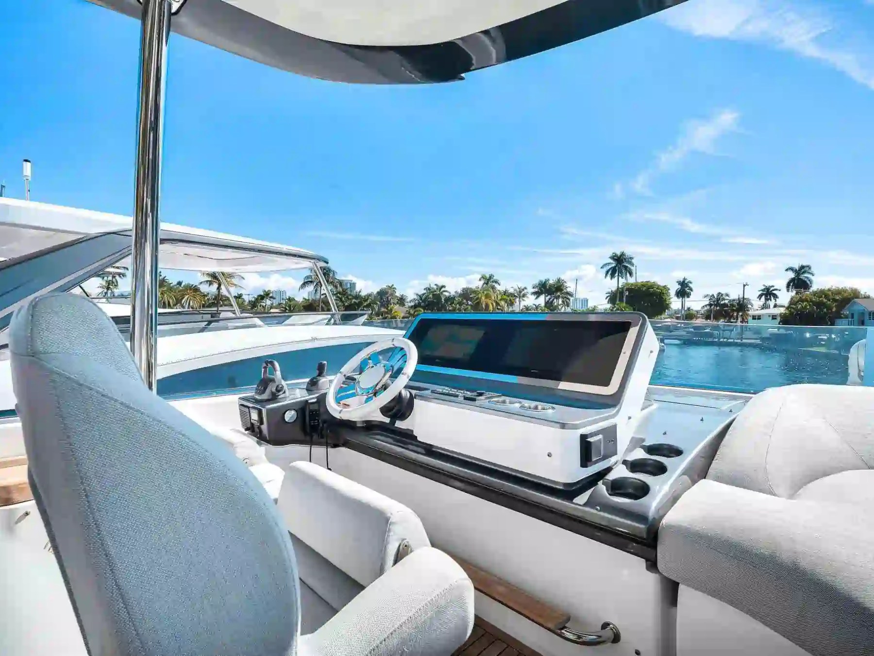 Boat cockpit with steering wheel and console overlooking water, palm trees, and blue sky.