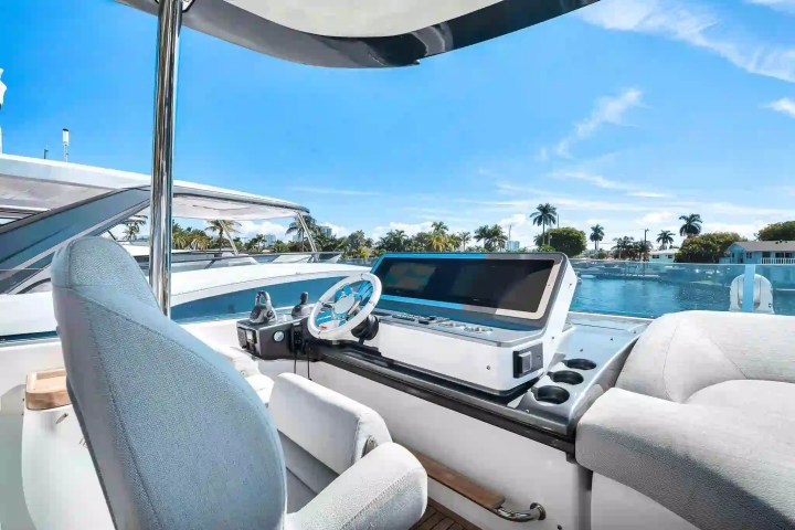 Boat cockpit with steering wheel and console overlooking water, palm trees, and blue sky.