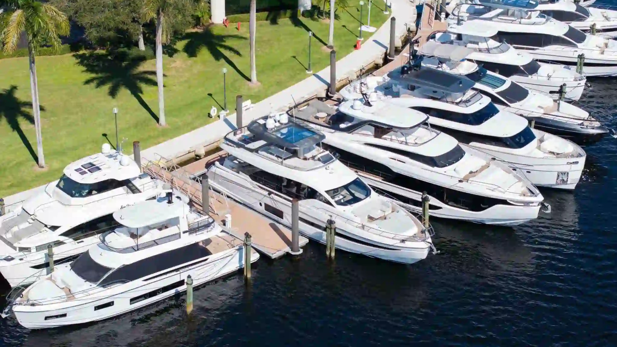 Aerial view of luxury yachts docked at a marina with palm trees nearby.