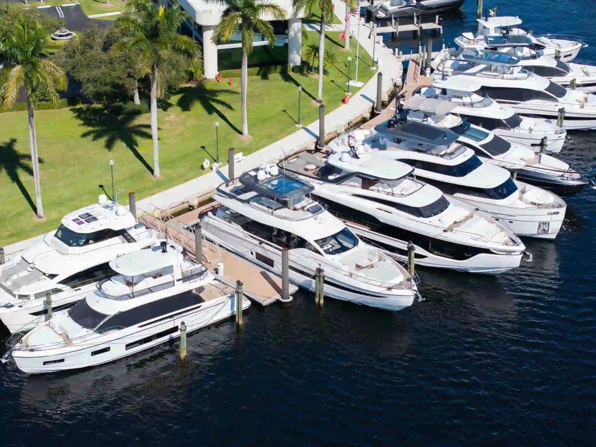 Aerial view of luxury yachts docked at a marina with palm trees nearby.