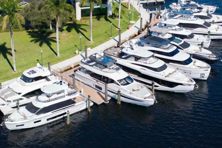 Aerial view of luxury yachts docked at a marina with palm trees nearby.
