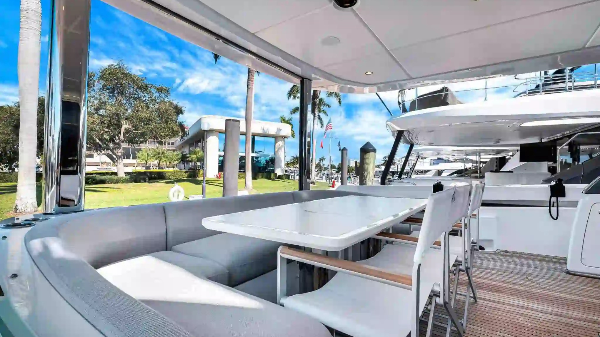 Outdoor yacht dining area with table, chairs, and sofa, overlooking dock and palm trees against a clear sky.